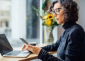 Frau schaut auf ihr Handy, Arbeit, Büro, Laptop